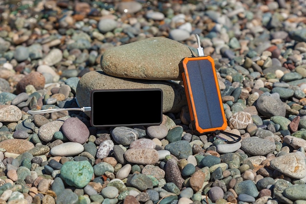 Le poverbank se trouve sur les galets au bord de la mer et charge le téléphone. Powerbank charge le téléphone.