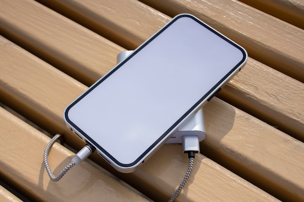 Power Bank charge une maquette de smartphone avec écran blanc sur un banc en bois dans le parc.