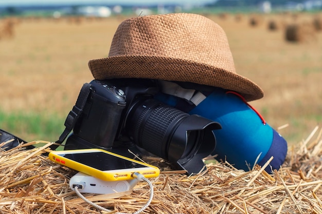 Power Bank charge un smartphone sur fond d'appareil photo avec un sac et un chapeau sur fond de foin dans la nature. Chargeur de voyage portable.