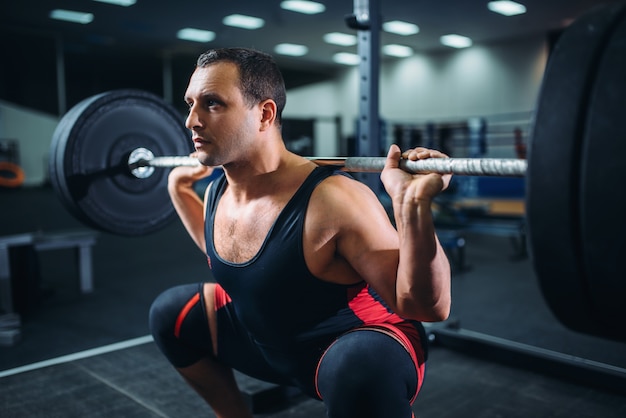 Powerlifter faisant des squats avec haltères dans une salle de sport