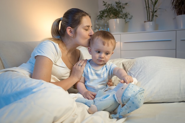 Pportrait de jeune mère embrassant son petit garçon avant d'aller dormir la nuit