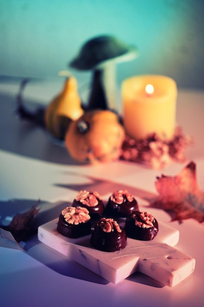 Pralinés au chocolat aux noix sur une planche à découper en marbre. Gros plan sur des bonbons. Arrangement d'automne avec bougie, citrouilles, champignons en bois et feuilles de ginkgo. Lumière naturelle du soleil, longues ombres