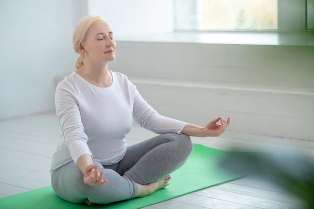 Pratique du yoga. Femme blonde mature assise en posture de lotus, méditant