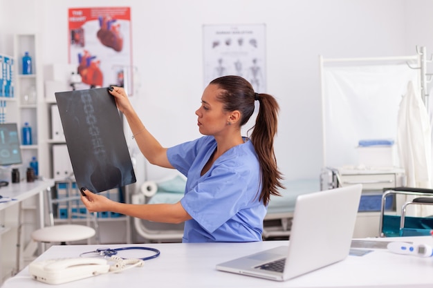 Pratique médicale examinant la radiographie d'un patient souffrant de problèmes de dos au bureau de l'hôpital. Radiologue en uniforme médical tenant et regardant les rayons X, l'examen, l'os, le praticien, l'analyse, le diagnostic