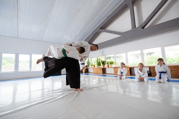 Pratiquer le lancer. Garçon aux cheveux noirs en kimono blanc pratiquant le lancer avec un entraîneur professionnel