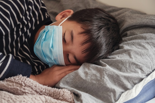 Préadolescent malade portant un masque et se reposant au lit