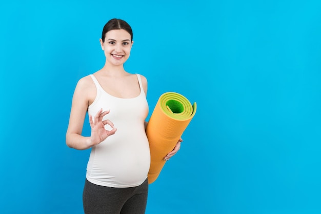 Pregnant Girl Holding Yoga Mat debout sur fond coloré Studio Shot Espace libre pour la conception