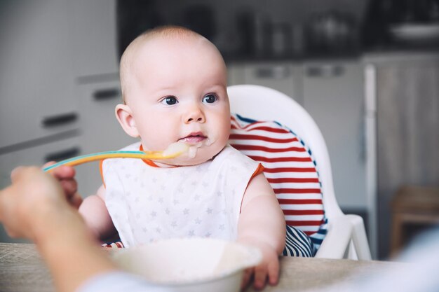 Premier aliment solide du bébé Mère nourrissant le petit enfant avec une cuillère de purée Routine quotidienne Nourriture avec les doigts