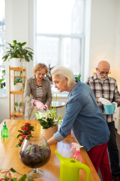 Premier. Belle femme âgée prenant une fleur tout en voulant la mettre dans le plus grand pot de fleurs