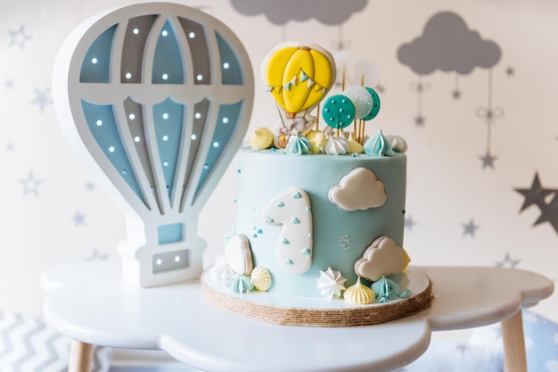 Premier gâteau d'anniversaire des enfants gâteau bleu avec des nuages de meringue et des ballons sur le fond des lumières de la chambre des enfants