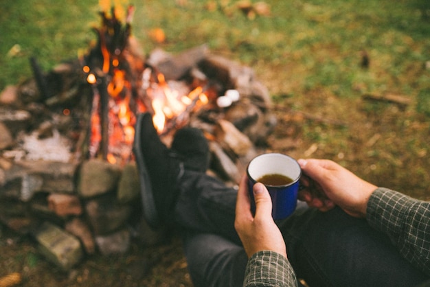 Premier point de vue. homme buvant du thé dans une tasse en métal près du feu de camp. randonnée