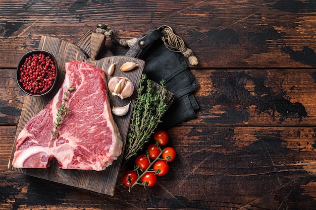 Premier steak de viande de boeuf Tbone bifteck d'aloyau cru sur planche de boucher avec des herbes fond en bois vue de dessus espace de copie