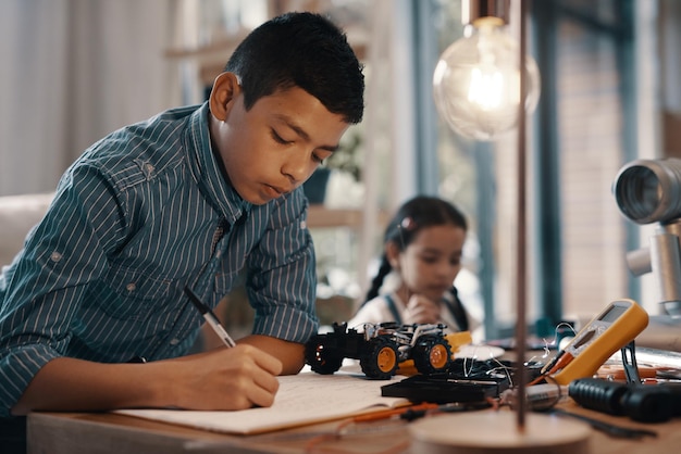 Premier temps de jeu après les devoirs Photo d'un beau jeune garçon faisant ses devoirs sur la robotique à la maison avec sa jeune sœur en arrière-plan