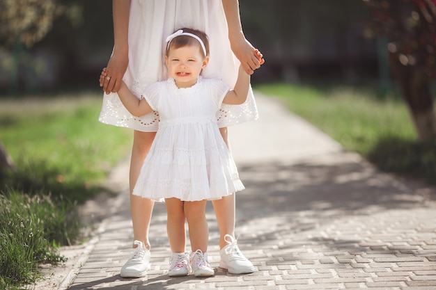 Premiers pas de bébé. Petit enfant essayant de marcher. Mère et sa petite fille adorable tenant par les mains. Mère et sa fille méconnaissables portant des baskets ou des keds