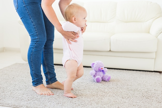 Premiers pas d'un bébé qui apprend à marcher dans un salon blanc et ensoleillé. Chaussures pour enfant.