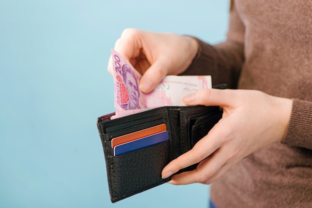 Prend de l'argent hryvnia ukrainienne d'un sac à main sur un fond bleu. concept de paiement.