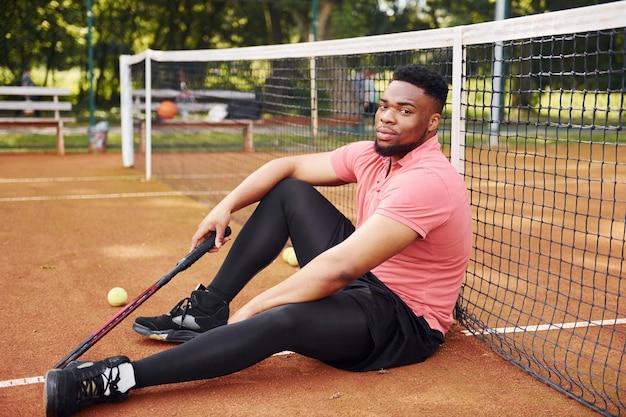 Prend une pause Un homme afro-américain en chemise rose joue au tennis sur le terrain à l'extérieur