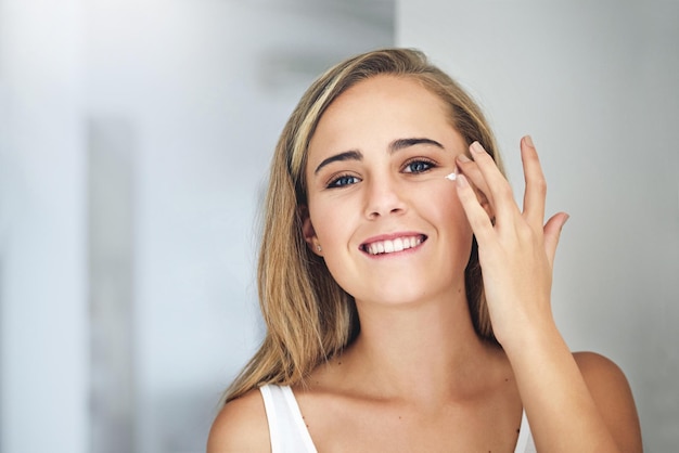 Prendre bien soin de sa peau Photo recadrée d'une jolie jeune femme appliquant une crème hydratante sur son visage dans la salle de bain