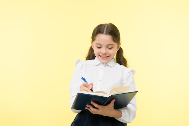 Prendre des notes. Enfant d'uniforme scolaire à faire ses devoirs. Les vêtements d'uniforme scolaire fille enfant tiennent un livre et un stylo. Fille mignonne écrivez des notes d'idée. Notes à retenir. Écrivez un essai ou des notes. Horaire personnel.