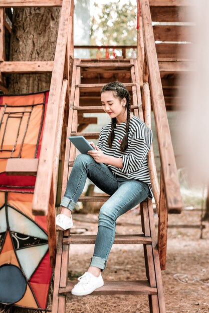 Prendre des notes. Enthousiaste femme brune assise sur les escaliers tout en regardant son gadget