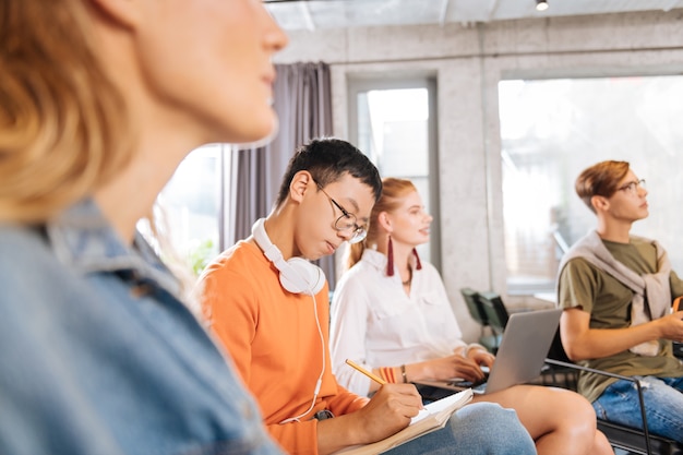 Prendre des notes. Étudiant international concentré assis en semi-position lors d'une conférence en visite