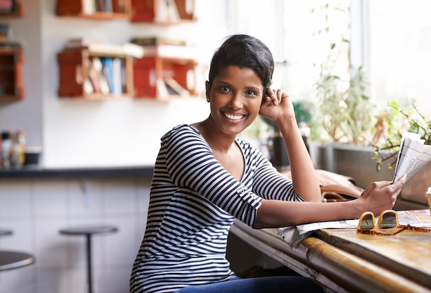 Prendre des nouvelles avec son café Une jeune femme assise dans un café avec un journal à la main