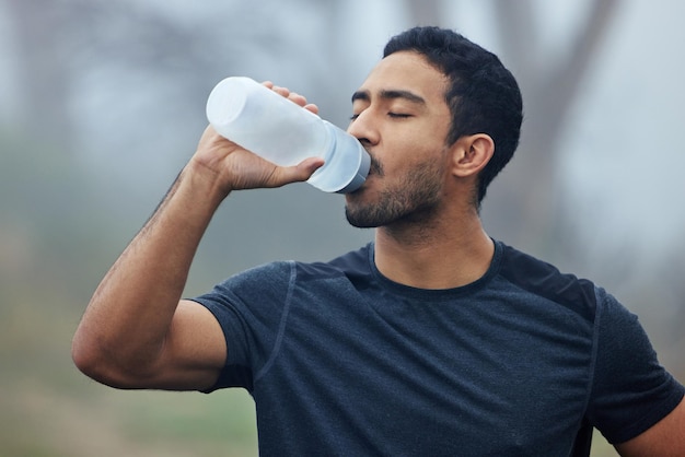 Prendre une pause pour reconstituer son énergie Photo d'un jeune homme sportif buvant de l'eau tout en faisant de l'exercice à l'extérieur