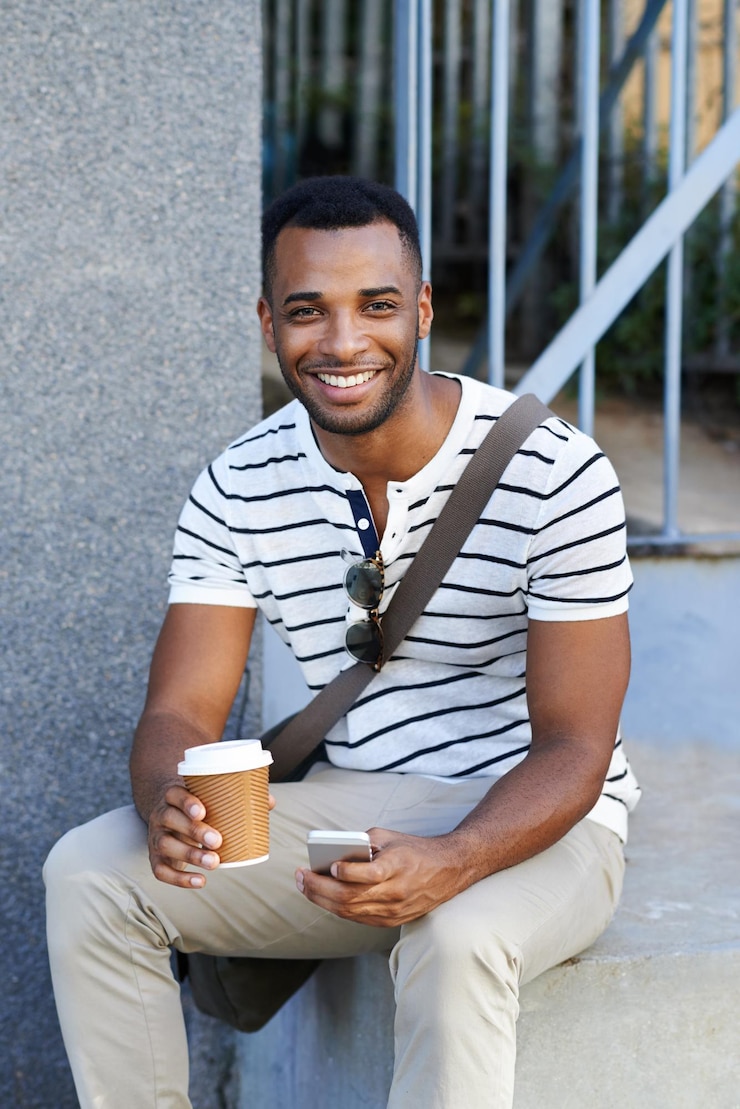 Photo prendre une pause rapide un bel homme d'affaires afro-américain habillé avec désinvolture assis dans la ville et utilisant son téléphone portable tout en buvant du café