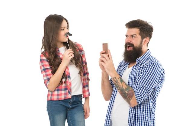 Prendre une photo Équipe créative Homme barbu prendre une photo d'un petit enfant Fille posant avec des accessoires de moustache Hipster utiliser un appareil photo mobile pour smartphone Fête de famille Séance photo de famille Objectifs familiaux