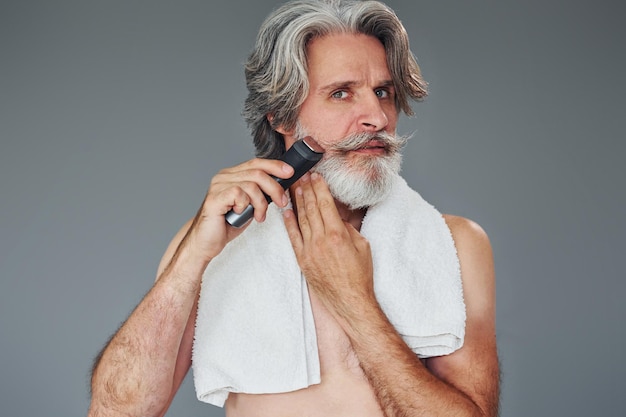 Prendre soin de la barbe Un homme âgé moderne et élégant aux cheveux gris est à l'intérieur