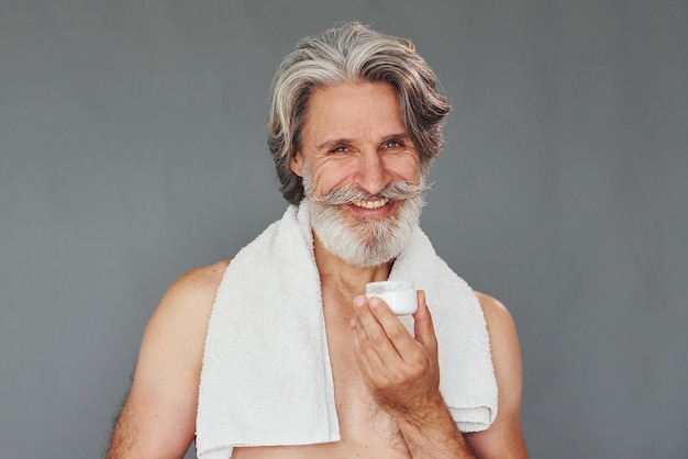 Prendre soin de la clarté du visage et de la peau Un homme senior moderne et élégant aux cheveux gris et à la barbe est à l'intérieur