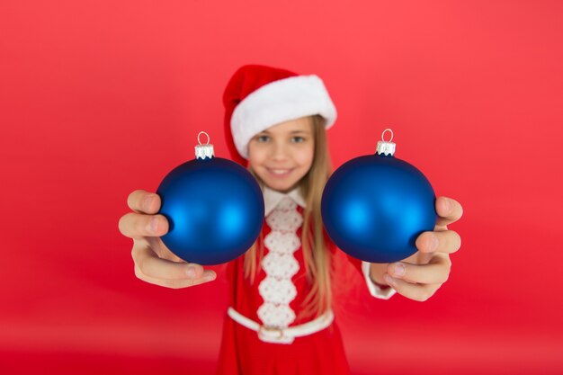 Prends-le. Créez des décorations uniques. Décor de boule de Noël. Idées de décoration de Noël pour la chambre des enfants. Le costume rouge d'enfant heureux tient des ornements de Noël se bouchent la mise au point sélective. Achetez des décorations.