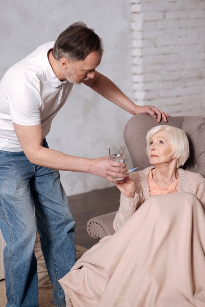 Prends-le. Gros plan d'un homme âgé se penchant vers sa femme âgée avec verre.