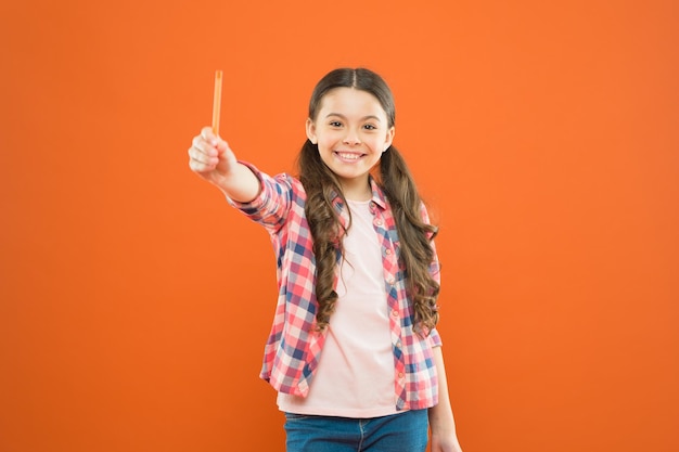 Prends mon stylo d'écriture Enfant d'école heureux apprécie ses compétences d'écrit Une petite fille ayant une tâche d'écrire sur un fond orange Pratique de la parole et de l'écriture