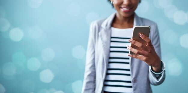 Photo prenez contact et réalisez-le. photo recadrée en studio d'une jeune femme d'affaires utilisant un téléphone portable sur fond bleu.