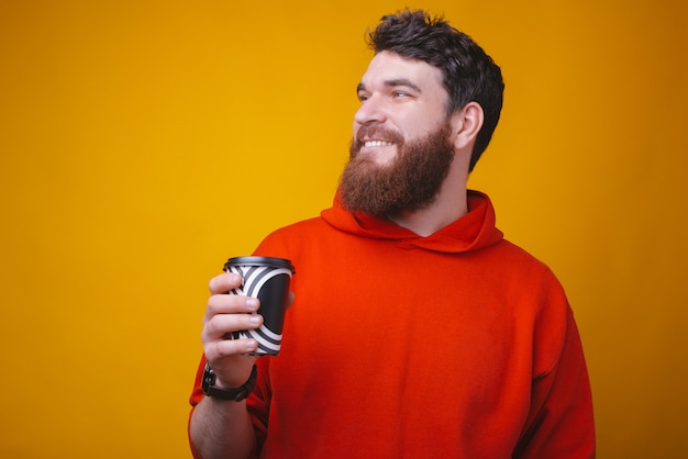 Prenez votre café pour partir. Photo d'un gars barbu tient un papier pour aller tasse de café sur l'espace jaune.