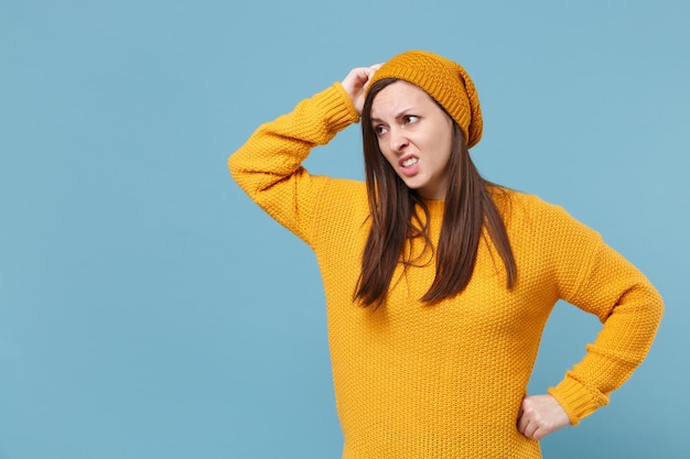 Préoccupée jeune femme brune fille en chapeau pull jaune posant isolé sur fond bleu portrait en studio. Concept de mode de vie des émotions sincères des gens. Maquette de l'espace de copie. Mettre la main sur la tête.