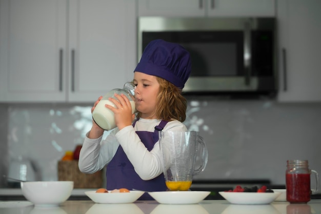 Préparation des aliments pour enfants petit chef préparant un repas sain mignon enfant garçon en uniforme de chef boire du lait sur