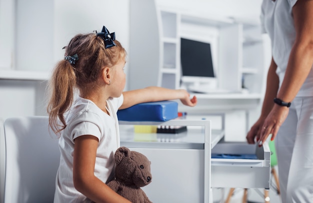 Préparation au prélèvement sanguin. Une petite fille avec son jouet en mains est à la clinique.