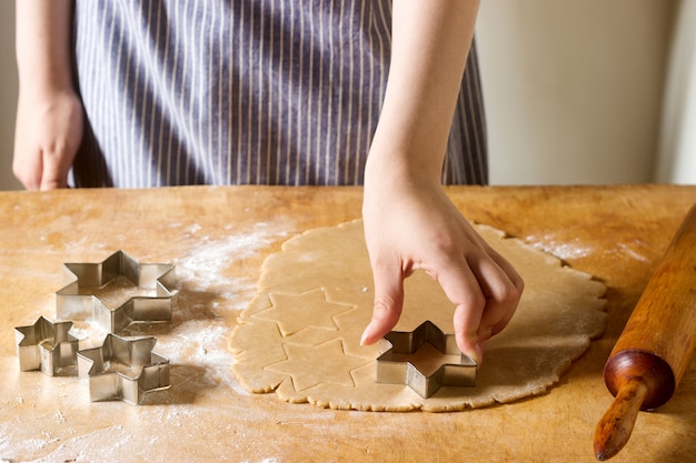Préparation de biscuits au gingembre. Une femme découpe des cookies en forme d'étoile. Pâtisserie, concept de cuisine maison.