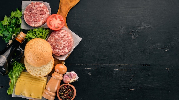 Préparation de burger Viande légumes frais tomates oignons Sur un fond en bois noir Vue de dessus Espace de copie gratuit