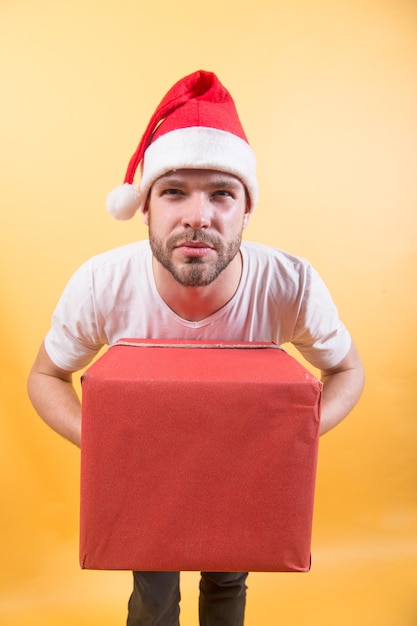 Préparation des cadeaux de Noël et du nouvel an. Père Noël avec boîte sur fond orange. Notion de lendemain de Noël. Macho au chapeau rouge tient un paquet cadeau emballé. Célébration des vacances d'hiver, espace de copie