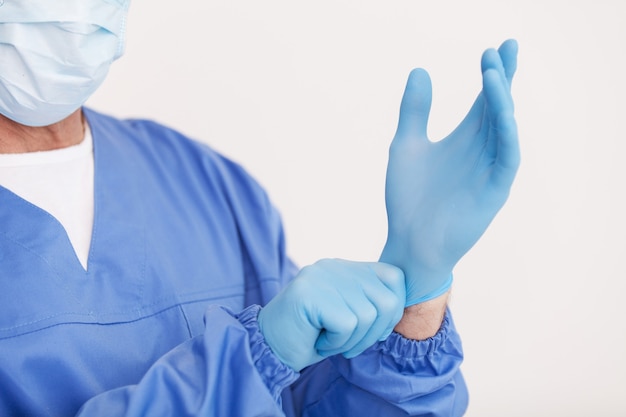 Photo préparation à la chirurgie. image recadrée d'un médecin portant un masque chirurgical ajustant son gant de protection en se tenant debout isolé sur blanc