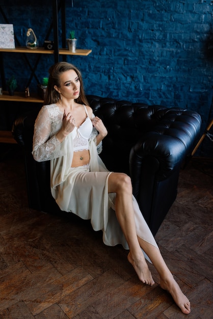 Préparation du matin de la mariée. Belle jeune femme en déshabillé de mariage blanc s'amuse dans un studio sombre