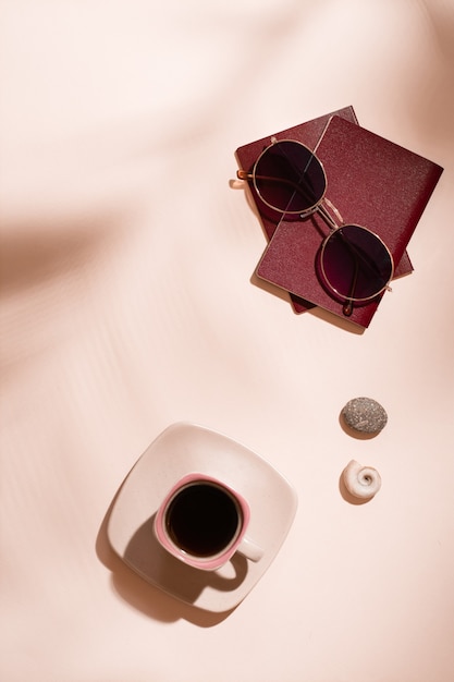 Préparation du voyage. Passeports, lunettes de soleil, coquillages et une tasse de café sur fond rose à l'ombre des feuilles des arbres. Tourisme local. Vue de dessus et verticale