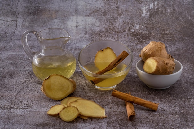 préparation d'une infusion de gingembre et de cannelle avec des racines naturelles de produits frais et un bâton de cannelle servi dans un pichet et une tasse