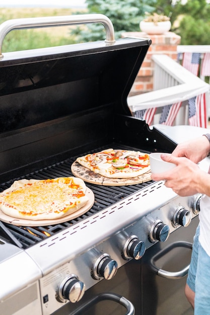 Préparation de pizzas grillées individuelles sur un gril à gaz extérieur.