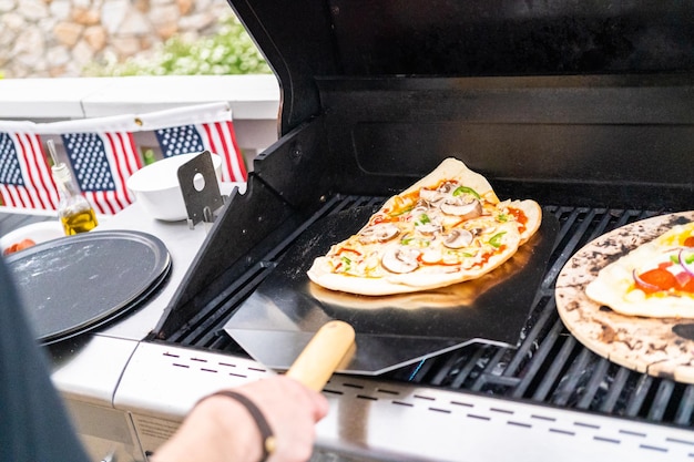 Préparation de pizzas grillées individuelles sur un gril à gaz extérieur.