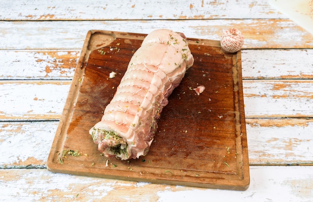 Photo préparation d'une porchetta avec un mélange d'herbes aromatiques posé sur un morceau de poitrine de porc frais ouvert dans l'épaisseur