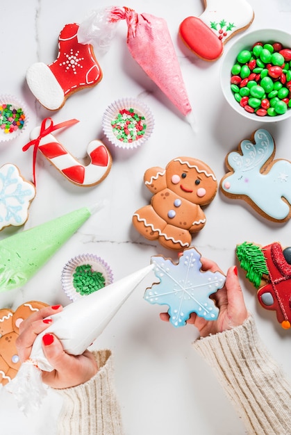 Préparation pour Noël, la jeune fille les mains sur la photo décore le pain d'épice traditionnel fait maison avec du sucre glace multicolore, des biscuits, une table en marbre blanc. vue de dessus